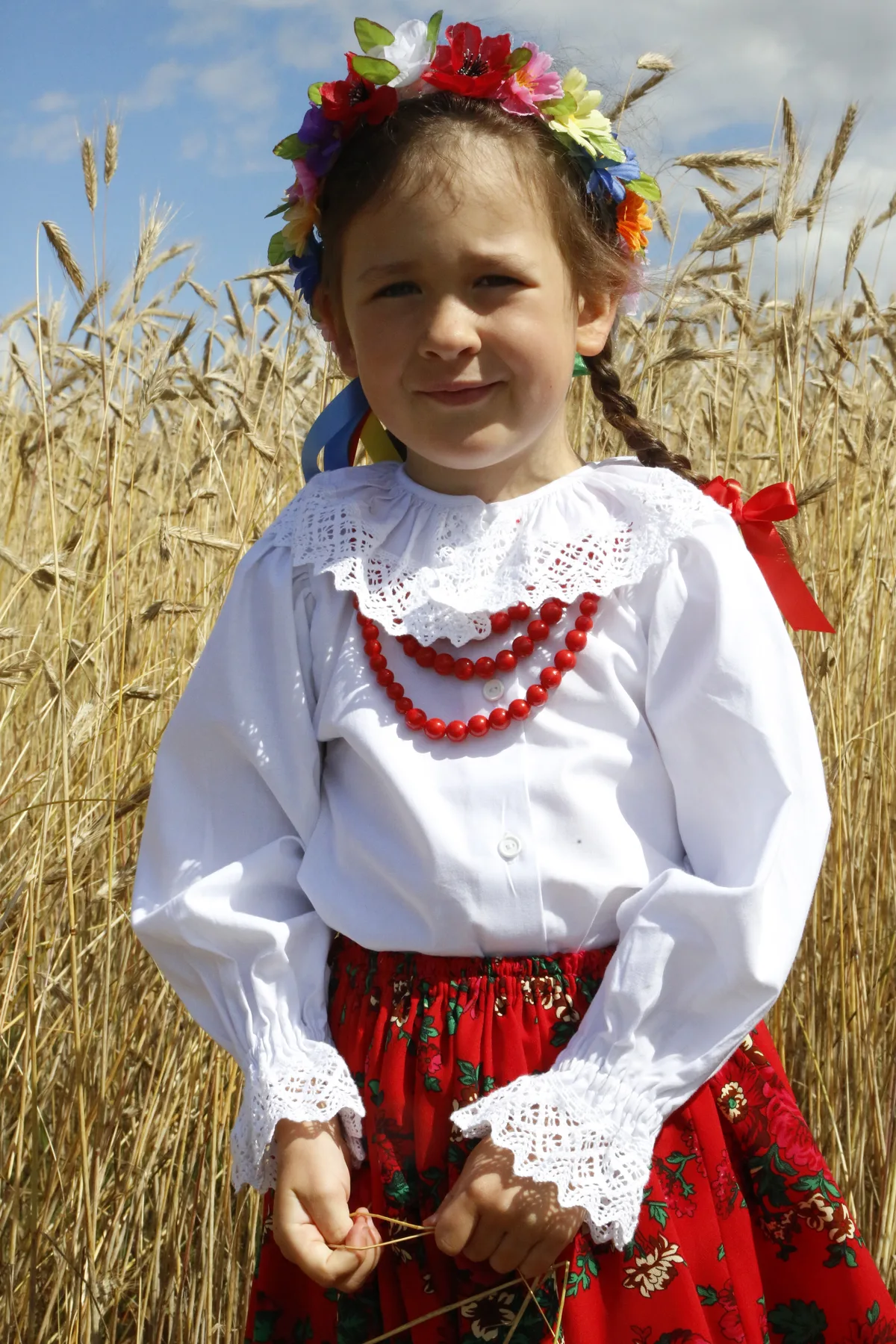 Dziewczynka w bluzce z długim rękawem, czerwonej spódniczce, koralach i wianku